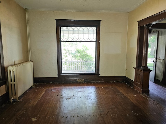 empty room with dark hardwood / wood-style flooring, radiator heating unit, crown molding, and ornate columns