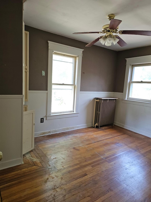 unfurnished room featuring hardwood / wood-style floors, ceiling fan, and radiator heating unit