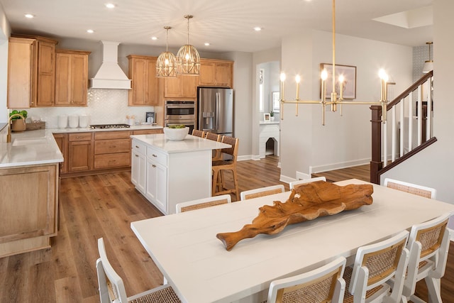 kitchen featuring premium range hood, light hardwood / wood-style floors, a kitchen island, pendant lighting, and stainless steel appliances