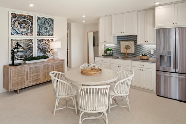 kitchen with white cabinets, dark stone counters, tasteful backsplash, sink, and stainless steel fridge