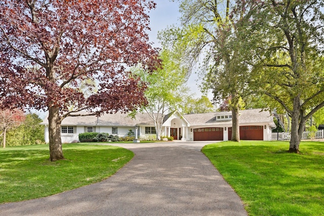 ranch-style house featuring driveway, a garage, fence, and a front lawn