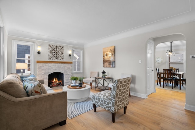 living room with light hardwood / wood-style flooring, ornamental molding, and a stone fireplace