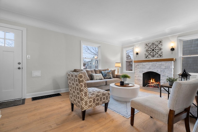 living room with crown molding, a stone fireplace, and light hardwood / wood-style flooring