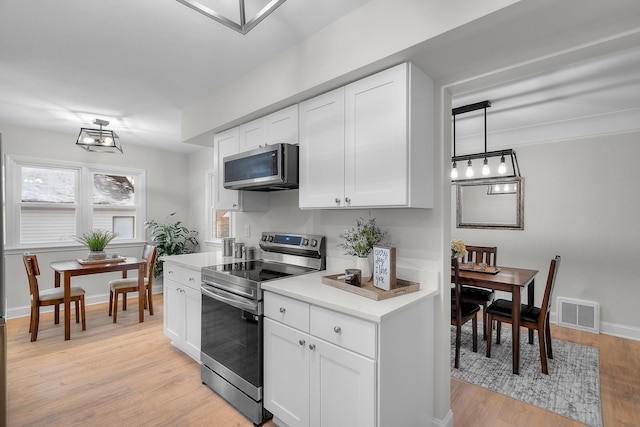 kitchen with hanging light fixtures, white cabinets, stainless steel appliances, and light wood-type flooring