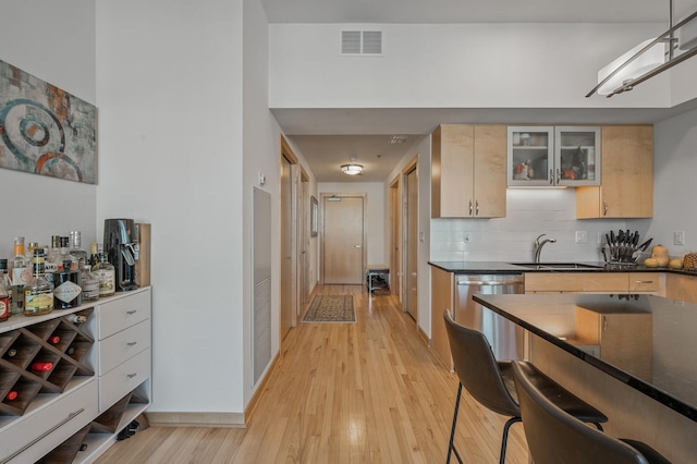 kitchen featuring light brown cabinets, sink, backsplash, stainless steel dishwasher, and light hardwood / wood-style flooring