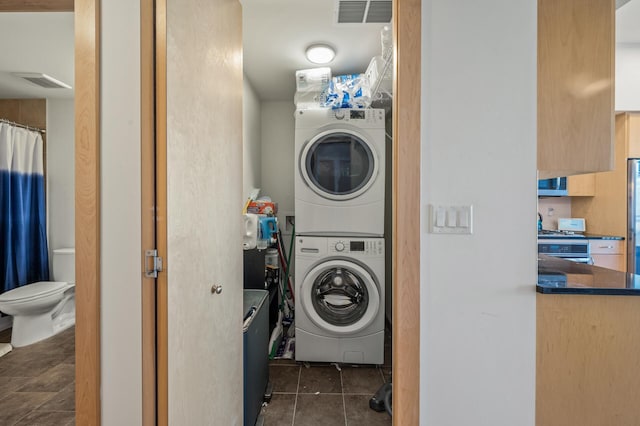 washroom with dark tile patterned flooring and stacked washer and clothes dryer