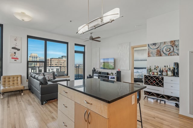 kitchen with a kitchen island, light brown cabinetry, light hardwood / wood-style floors, ceiling fan, and a breakfast bar