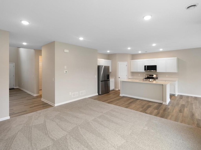 kitchen with white cabinets, appliances with stainless steel finishes, light carpet, sink, and a kitchen island with sink