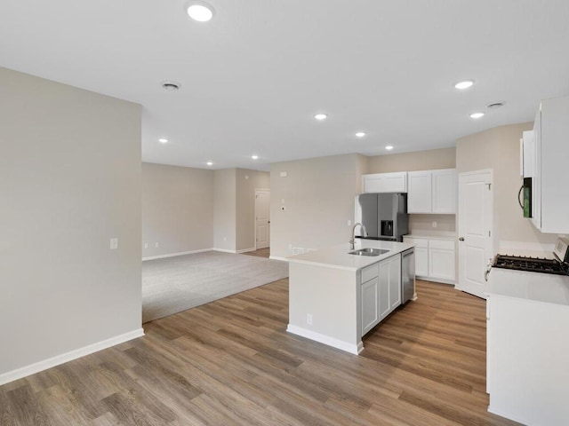 kitchen with appliances with stainless steel finishes, a kitchen island with sink, light wood-type flooring, white cabinets, and sink