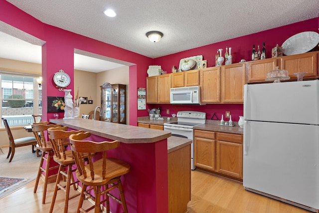 kitchen with light wood finished floors, a textured ceiling, white appliances, a peninsula, and a kitchen bar