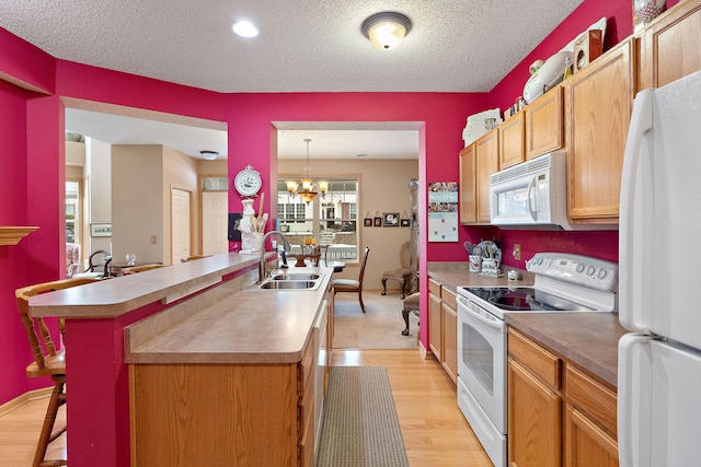 kitchen featuring a chandelier, a textured ceiling, white appliances, a sink, and light wood finished floors