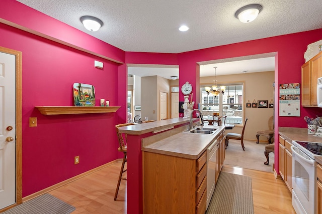 kitchen featuring white appliances, light wood-style flooring, an inviting chandelier, a kitchen bar, and a sink