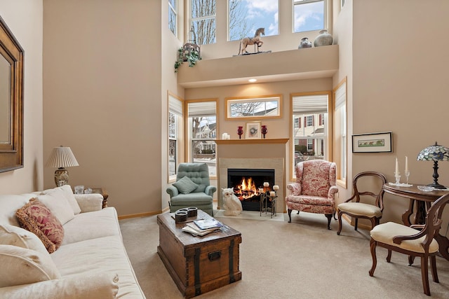 living room with a fireplace with flush hearth, carpet flooring, a towering ceiling, and baseboards