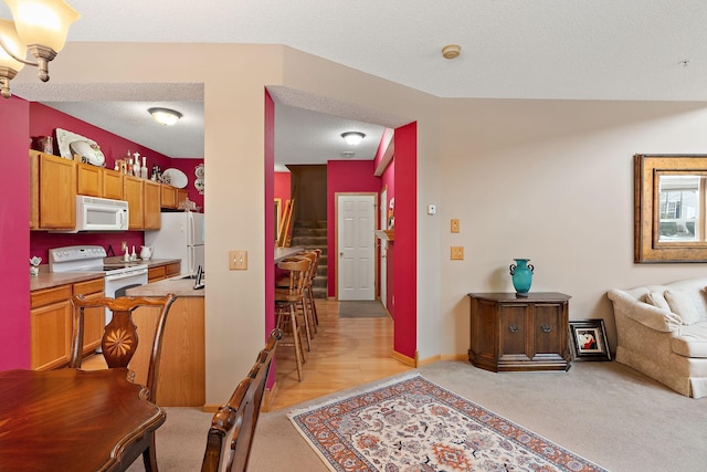 kitchen featuring a textured ceiling, light carpet, white appliances, open floor plan, and light countertops