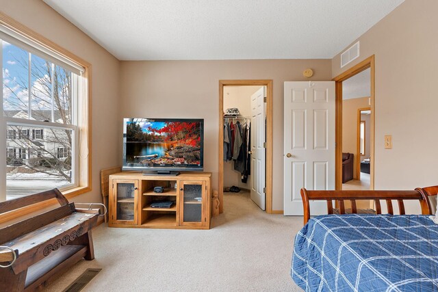 bedroom with a closet, light colored carpet, visible vents, a spacious closet, and a textured ceiling