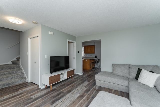 living room featuring dark wood-style floors, stairs, baseboards, and a textured ceiling