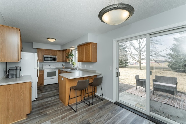 kitchen featuring brown cabinets, dark wood finished floors, white range with electric cooktop, stainless steel microwave, and a peninsula