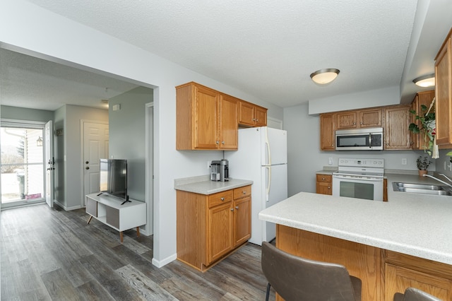 kitchen with a peninsula, white appliances, dark wood-style flooring, a breakfast bar, and a sink