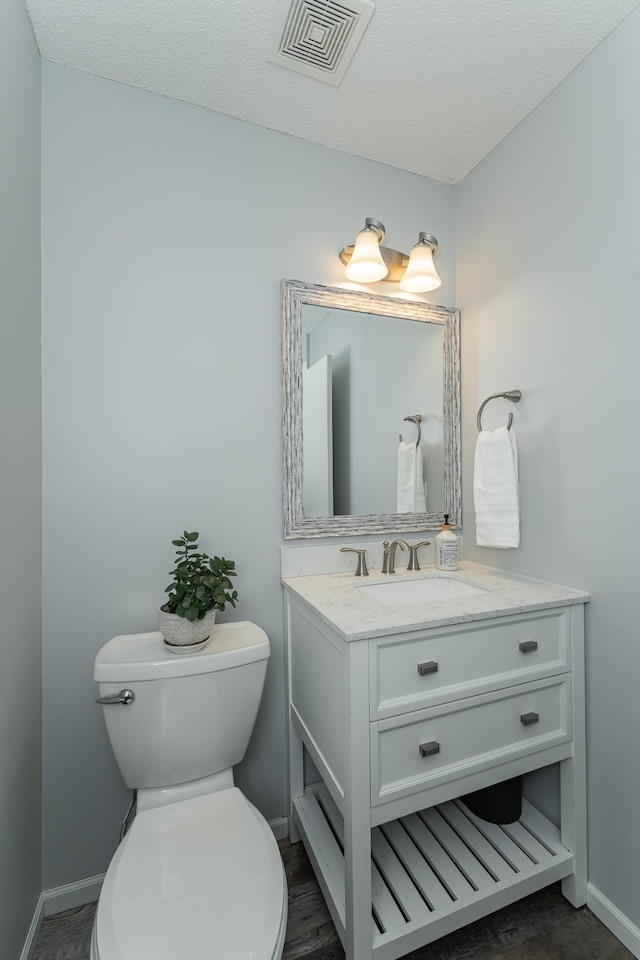 half bathroom featuring baseboards, visible vents, toilet, a textured ceiling, and vanity