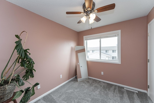 carpeted spare room featuring visible vents, baseboards, and ceiling fan