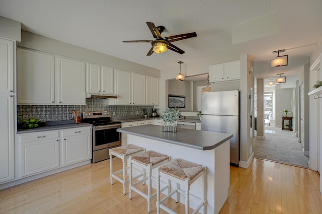 kitchen with dark countertops, tasteful backsplash, light wood-style flooring, appliances with stainless steel finishes, and white cabinetry