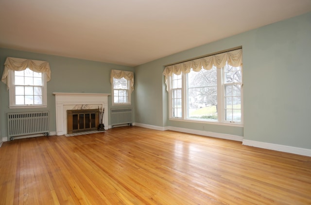 unfurnished living room featuring light hardwood / wood-style flooring, a high end fireplace, and radiator heating unit