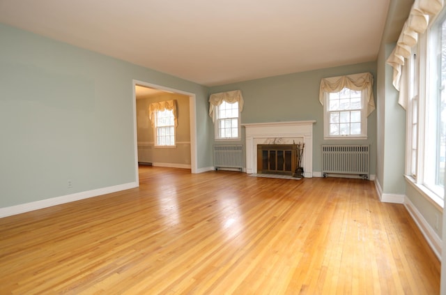 unfurnished living room featuring a fireplace, radiator, and light hardwood / wood-style floors