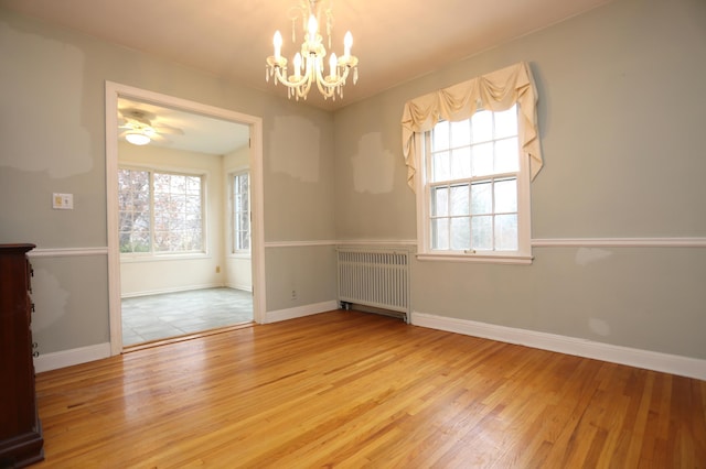 unfurnished room featuring radiator, ceiling fan with notable chandelier, and light wood-type flooring