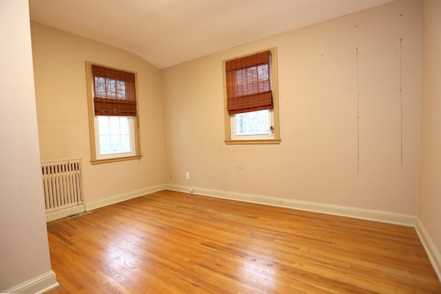 spare room featuring vaulted ceiling, radiator heating unit, and light hardwood / wood-style flooring