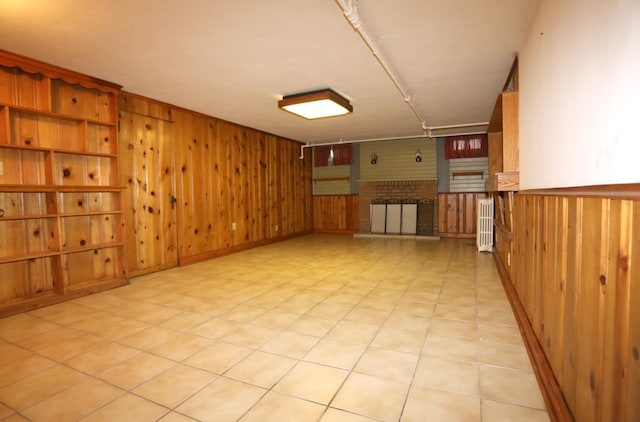 tiled empty room with wooden walls, radiator, and a brick fireplace