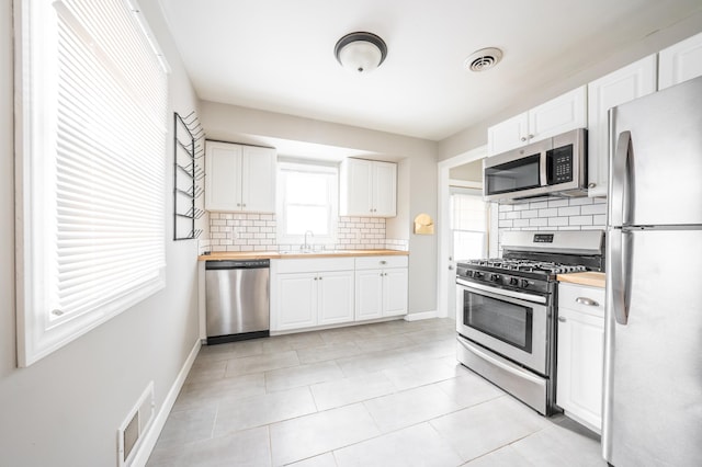 kitchen with appliances with stainless steel finishes, butcher block counters, sink, white cabinets, and backsplash