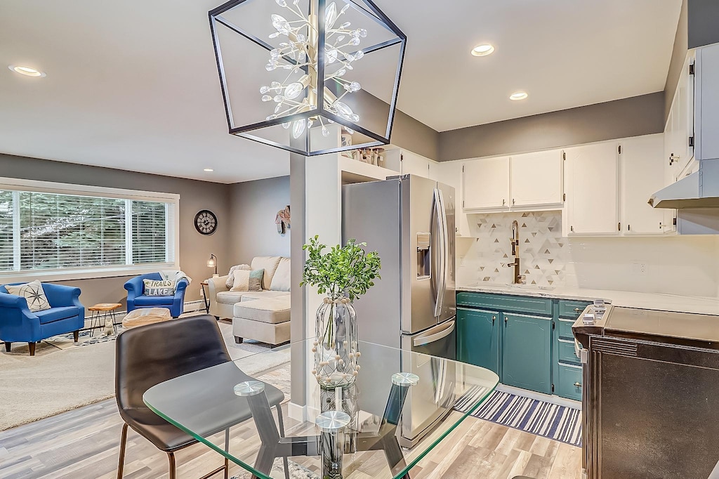 kitchen featuring sink, white cabinets, an inviting chandelier, tasteful backsplash, and stainless steel refrigerator with ice dispenser