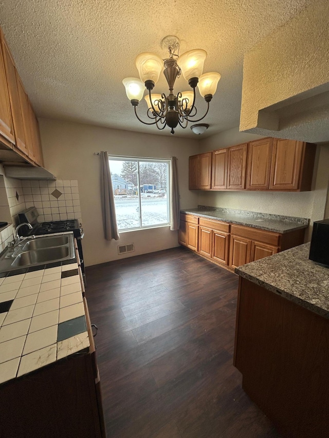 kitchen featuring decorative backsplash, dark wood-type flooring, sink, pendant lighting, and a notable chandelier