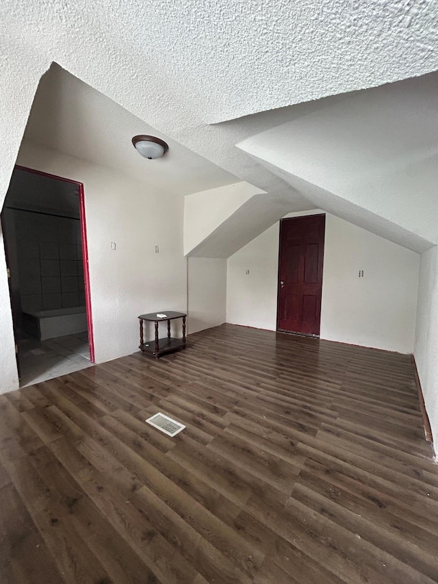 bonus room featuring lofted ceiling, dark wood-type flooring, and a textured ceiling