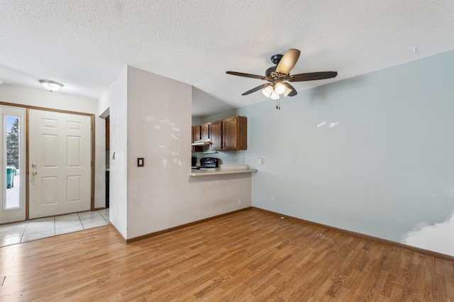 unfurnished living room featuring ceiling fan, a textured ceiling, and light wood-type flooring