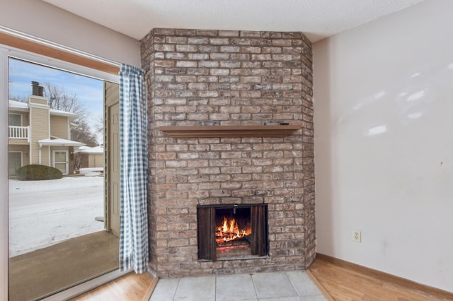 unfurnished living room featuring a textured ceiling, a brick fireplace, and light hardwood / wood-style flooring