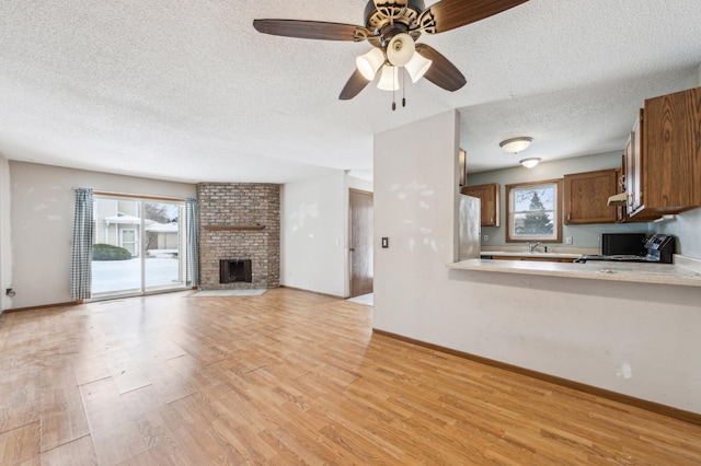 unfurnished living room with a brick fireplace, ceiling fan, a textured ceiling, and light wood-type flooring