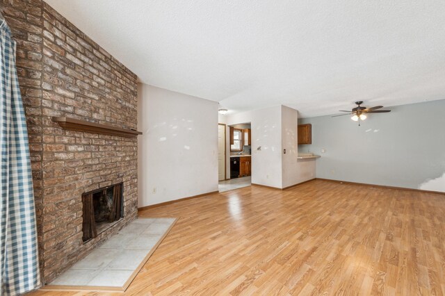 unfurnished living room featuring ceiling fan, a fireplace, light hardwood / wood-style flooring, and a textured ceiling