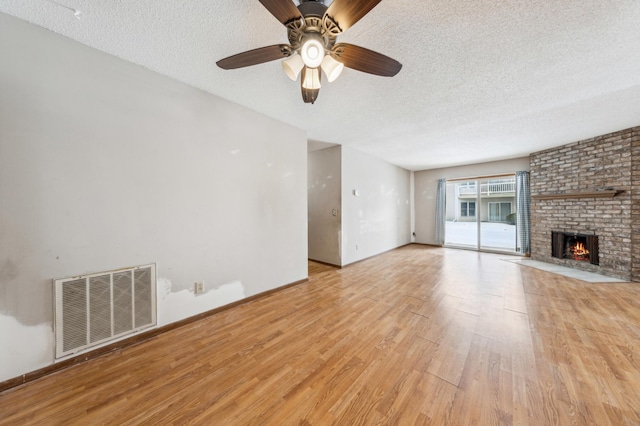 unfurnished living room featuring ceiling fan, a textured ceiling, a brick fireplace, and light wood-type flooring