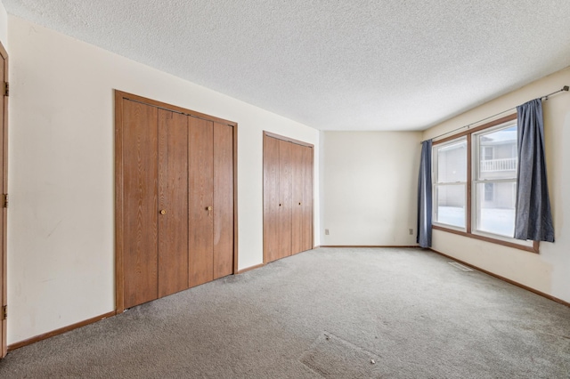 unfurnished bedroom featuring multiple closets, light colored carpet, and a textured ceiling