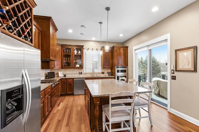 kitchen featuring decorative light fixtures, a kitchen breakfast bar, light wood-type flooring, a kitchen island, and appliances with stainless steel finishes