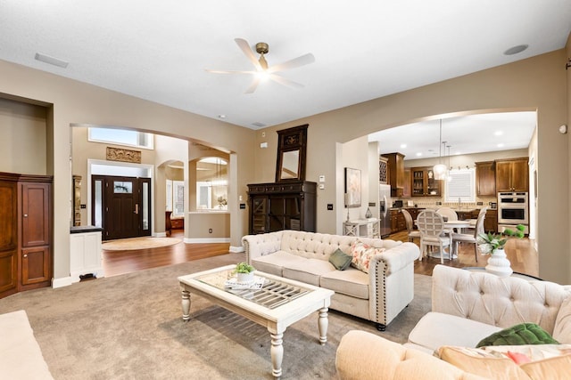 carpeted living room featuring ceiling fan with notable chandelier and a wealth of natural light