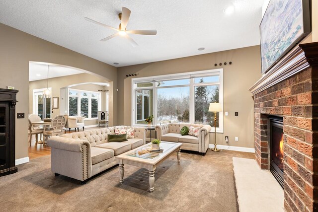 carpeted living room featuring a fireplace, a textured ceiling, and ceiling fan