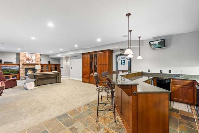 kitchen with a kitchen breakfast bar, a stone fireplace, dishwasher, dark colored carpet, and pendant lighting