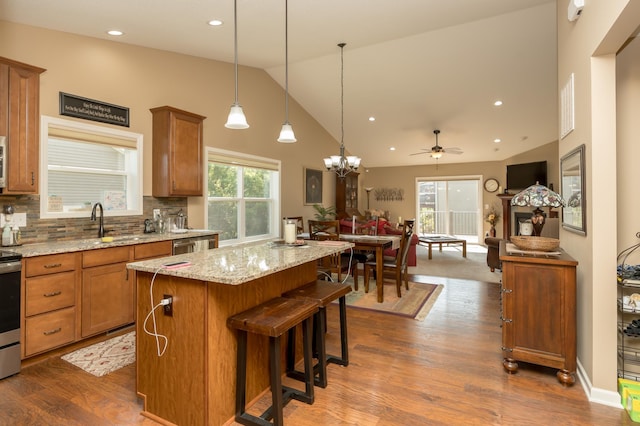 kitchen featuring ceiling fan with notable chandelier, vaulted ceiling, tasteful backsplash, decorative light fixtures, and a kitchen island