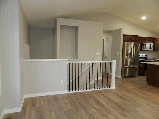 kitchen featuring stainless steel appliances, vaulted ceiling, dark brown cabinets, and hardwood / wood-style floors