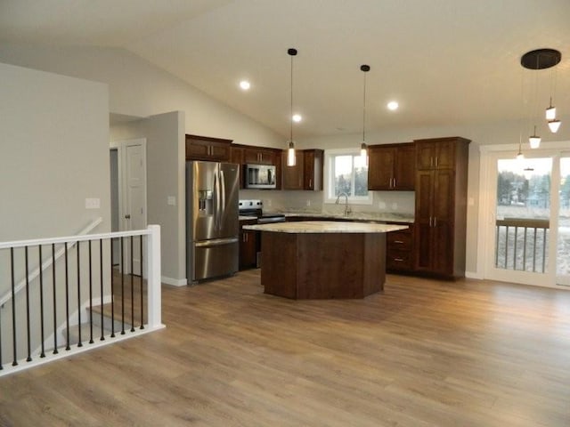 kitchen with appliances with stainless steel finishes, decorative light fixtures, a kitchen island, and light hardwood / wood-style flooring