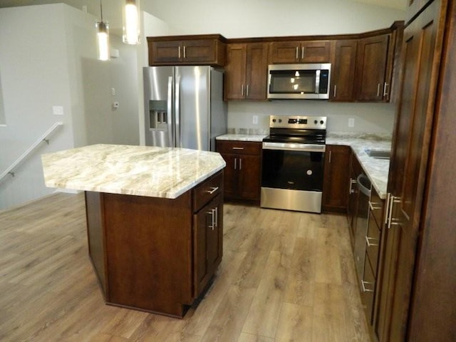 kitchen with stainless steel appliances, a center island, light stone counters, and light hardwood / wood-style flooring