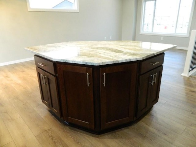 kitchen with light stone countertops, a kitchen island, dark brown cabinets, and light hardwood / wood-style floors