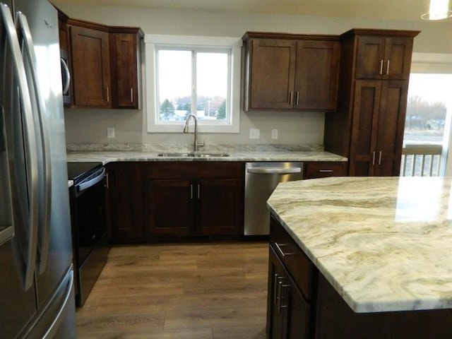 kitchen featuring stainless steel appliances, light stone countertops, sink, and wood-type flooring